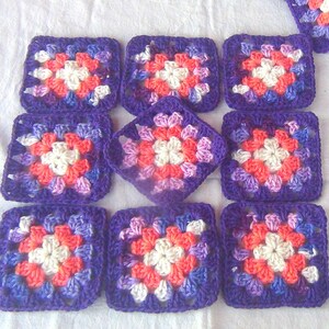 May include: Nine purple crochet squares with a white, pink, and orange flower design in the center of each square.