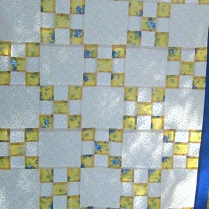 May include: A white and yellow quilt with a blue border. The quilt is made of squares and has a pattern of small white dots on the white squares.