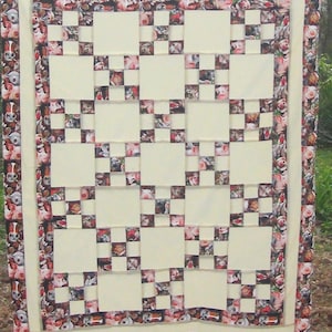 May include: A white quilt with a patchwork design. The quilt is made up of squares of white fabric with a border of squares of fabric with a piglet pattern.