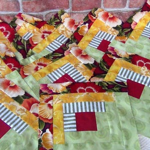 May include: A collection of patchwork fabric squares in shades of green, yellow, red, and white. The squares are sewn together to create a pattern of overlapping squares. The fabric features a floral print with red and white flowers.