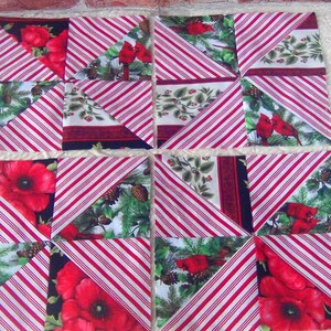 May include: A red and white striped fabric quilt block with a Christmas theme. The block features red cardinals, pine cones, and holly leaves. The block is made up of nine smaller squares, each with a different design.