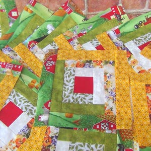 May include: A quilt block with a log cabin pattern in shades of green, yellow, and red. The block is made of squares of fabric sewn together to create a layered effect.