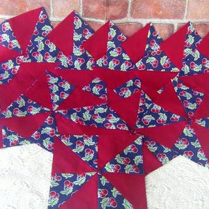 May include: A collection of red and blue fabric pieces arranged in a geometric pattern. The blue fabric features a white polka dot design with red cherries and green leaves. The red fabric forms the background.