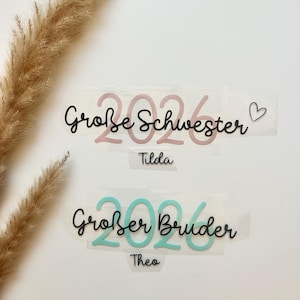 Könnte beinhalten: Zwei Aufbügelbilder aus Vinyl mit schwarzer Schreibschrift und farbigen Zahlen. Das obere Motiv zeigt Große Schwester 2026 mit einem Herz und dem Namen Tilda. Das untere Motiv zeigt Großer Bruder 2026 mit dem Namen Theo in schwarzer Schrift.