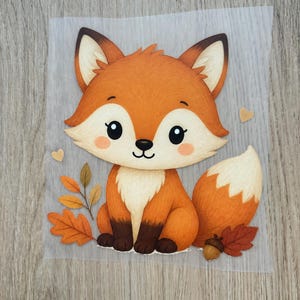 Könnte beinhalten: Ein dekorativer Transfer mit einem Cartoon-Fuchs mit orangefarbenem Fell, weißer Brust und dunkelbraunen Pfoten. Der Fuchs ist von herbstlichen Elementen umgeben, darunter orangefarbene und braune Blätter, eine kleine braune Eichel und zwei kleine Herzen.