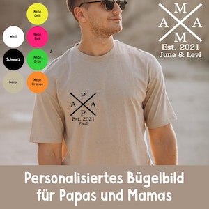 Könnte beinhalten: Ein beiges T-Shirt mit einem schwarzen Grafikdesign auf der Vorderseite und dem Text "A P A P Est. 2021 Paul". Das Shirt hat auch ein Design auf der Rückseite mit dem Text "M A M A Est. 2021 Juna & Levi". Das Bild enthält Farbmuster.