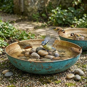 May include: A round, shallow bird bath with a hammered copper interior and a weathered, teal-patina exterior. The basin is filled with water and smooth, rounded river stones, with several small birds bathing and splashing in the water.