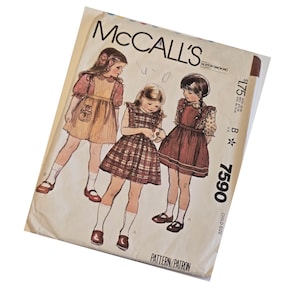 May include: Vintage McCall's sewing pattern for child-sized dresses. The pattern envelope features illustrations of three young girls wearing different dress designs. The text "McCall's" is prominently displayed at the top, with the pattern number 7590 visible.