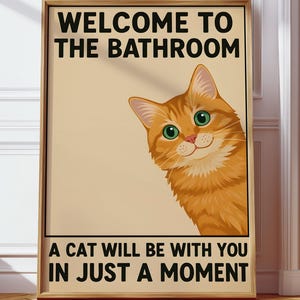 May include: Framed poster with the text "WELCOME TO THE BATHROOM" and "A CAT WILL BE WITH YOU IN JUST A MOMENT." The poster features a cartoon orange tabby cat with green eyes. The poster is in a wooden frame and is leaning against a wall.