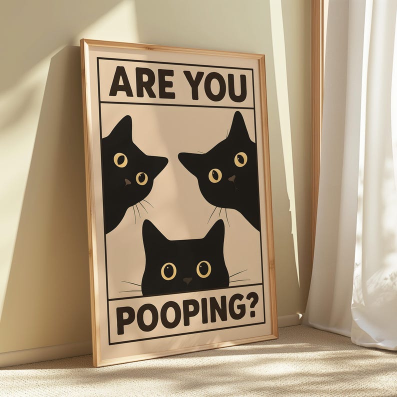 May include: A framed art print featuring three black cat silhouettes with yellow eyes on a beige background. The text "ARE YOU" is above the cats, and "POOPING?" is below. The frame is a light wood color.