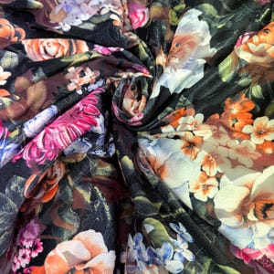 May include: Close-up of a fabric with a floral pattern. The fabric features a dark background with a variety of flowers in shades of orange, pink, white, and purple. The fabric is folded and draped.