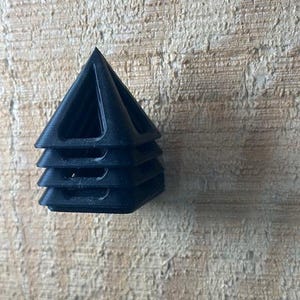 May include: A stack of four black, pyramid-shaped objects. Each pyramid has a triangular base and a hollow center. The objects are stacked on top of each other, with the points of the pyramids facing upwards.