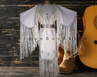 May include: A white fringed dress with a matching shawl, adorned with beads and a decorative belt. A guitar and cowboy boots are in the background, suggesting a Western or bohemian theme.