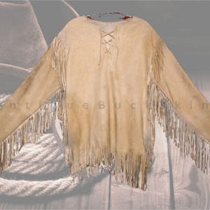 Peut inclure: Une chemise en daim beige avec des manches longues et des franges le long des manches et de l'ourlet. Le dos de la chemise présente un motif lacé. Le texte "antique buckskin" est visible sur la chemise.