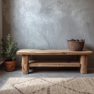 Könnte beinhalten: Rustikale Holzbank mit unterem Regal, vor einer strukturierten grauen Wand. Ein geflochtener Korb mit Tannenzapfen steht auf der Bank. Eine kleine Topfpflanze und ein gemusterter Teppich befinden sich im Vordergrund.
