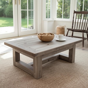May include: A rectangular, gray wooden coffee table with a rustic design. A wooden bowl filled with nuts and a white teacup and saucer sit on the table. The table is 48 inches long and 24 inches wide.