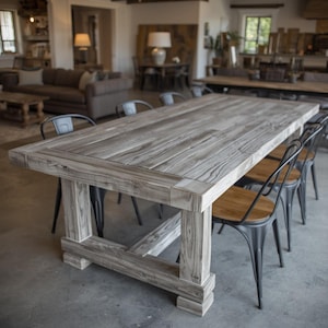 Könnte beinhalten: Ein großer, rechteckiger Esstisch aus Holz mit verwitterter grauer Oberfläche. Der Tisch hat ein stabiles Gestell und ist von Metallstühlen mit Holzsitzen umgeben. Der Tisch ist etwa 244 cm lang und 102 cm breit.