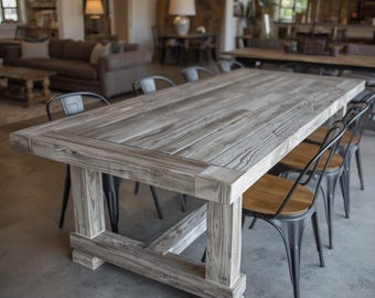 Könnte beinhalten: Ein rechteckiger Esstisch aus verwitterten grauen Holzplanken mit einem dicken, stabilen Rahmen und vier massiven Beinen. Der Tisch ist von mehreren schwarzen Metallstühlen mit abgerundeten Rückenlehnen und Holzsitzflächen umgeben.