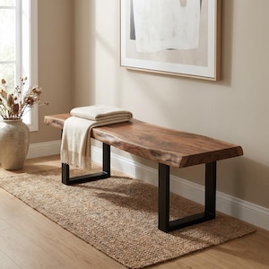 May include: A wooden bench with a natural live edge top and a smooth brown wood grain finish. The bench is supported by two rectangular black metal legs. A folded cream-coloured throw blanket with fringe edges rests on the seat of the bench.