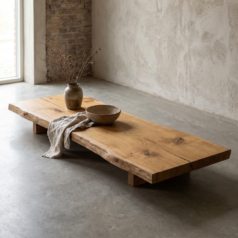 May include: A low-profile rectangular coffee table crafted from a single slab of natural light brown wood with a live edge. The table features a visible wood grain, a central crack, and short block legs. A ceramic vase and bowl sit on top.