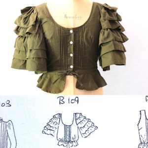Op de afbeelding: Een groene, korte mouwen blouse met een gerimpelde halslijn en meerdere lagen ruches op de mouwen. De blouse heeft een getailleerd lijfje en een geplooide rok. De blouse is in de taille gebonden met een lint. De blouse is gemarkeerd met "B 109".
