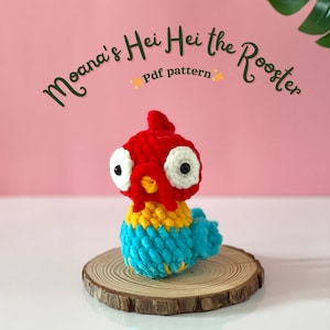 Peut inclure: Un Hei Hei le Coq au crochet fait à la main, du film Moana, en rouge, jaune et bleu. Le coq est posé sur une tranche de bois. Le texte "Moana's Hei Hei the Rooster PDF pattern" est arqué au-dessus du coq.