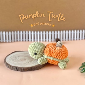 以下が含まれることがあります： カボチャに似た、オレンジと緑色の手編みのカメ。カメは緑色の頭と足、オレンジ色の体、小さな茶色の茎をしています。「Pumpkin Turtle」と「Pdf pattern」の文字が画像に含まれています。