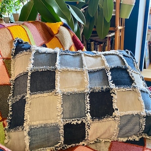 Pode incluir: Uma almofada de patchwork feita de tecido de ganga com bordas desfiadas. A almofada está sentada em uma manta de malha colorida.