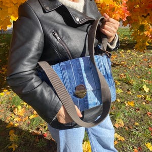 Upcycled denim messenger bag with striped design, adjustable strap, black nylon lining, and 2 interior pockets.