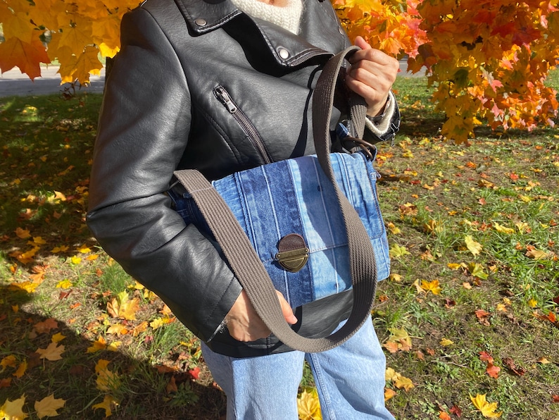 Upcycled denim messenger bag with striped design, adjustable strap, black nylon lining, and 2 interior pockets.