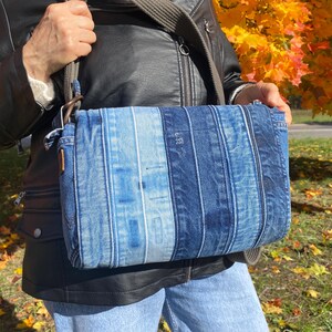 Upcycled denim messenger bag with striped design, adjustable strap, black nylon lining, and 2 interior pockets.