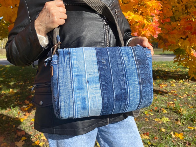 Upcycled denim messenger bag with striped design, adjustable strap, black nylon lining, and 2 interior pockets.