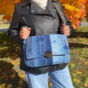 Upcycled denim messenger bag with striped design, adjustable strap, black nylon lining, and 2 interior pockets.