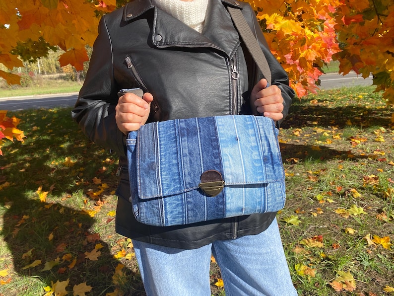 Upcycled denim messenger bag with striped design, adjustable strap, black nylon lining, and 2 interior pockets.
