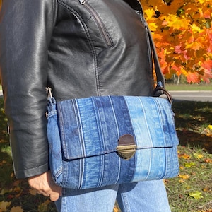 Upcycled denim messenger bag with striped design, adjustable strap, black nylon lining, and 2 interior pockets.