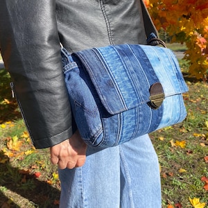 Upcycled denim messenger bag with striped design, adjustable strap, black nylon lining, and 2 interior pockets.