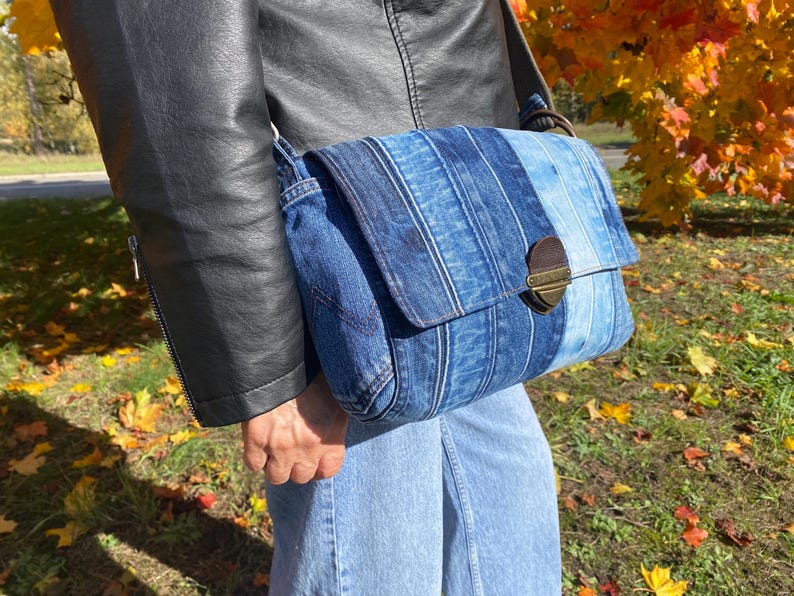 Upcycled denim messenger bag with striped design, adjustable strap, black nylon lining, and 2 interior pockets.