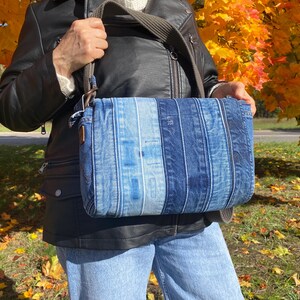 Upcycled denim messenger bag with striped design, adjustable strap, black nylon lining, and 2 interior pockets.
