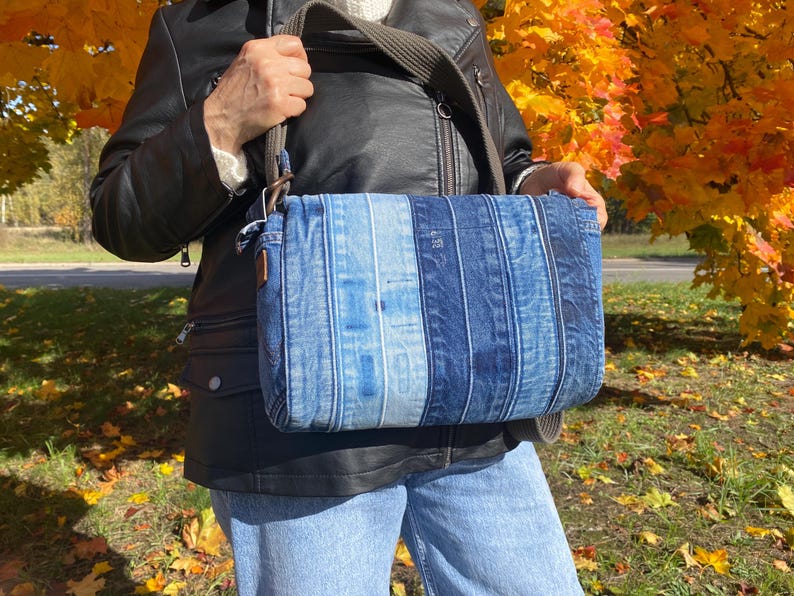 Upcycled denim messenger bag with striped design, adjustable strap, black nylon lining, and 2 interior pockets.