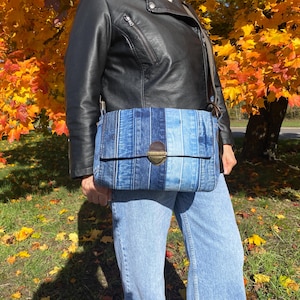 Upcycled denim messenger bag with striped design, adjustable strap, black nylon lining, and 2 interior pockets.