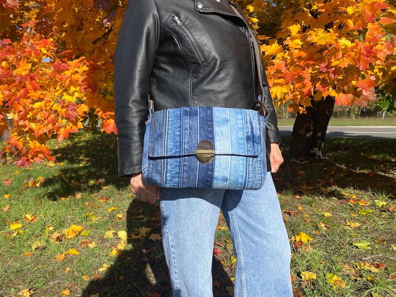 Upcycled denim messenger bag with striped design, adjustable strap, black nylon lining, and 2 interior pockets.