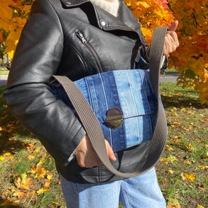 Upcycled denim messenger bag with striped design, adjustable strap, black nylon lining, and 2 interior pockets.