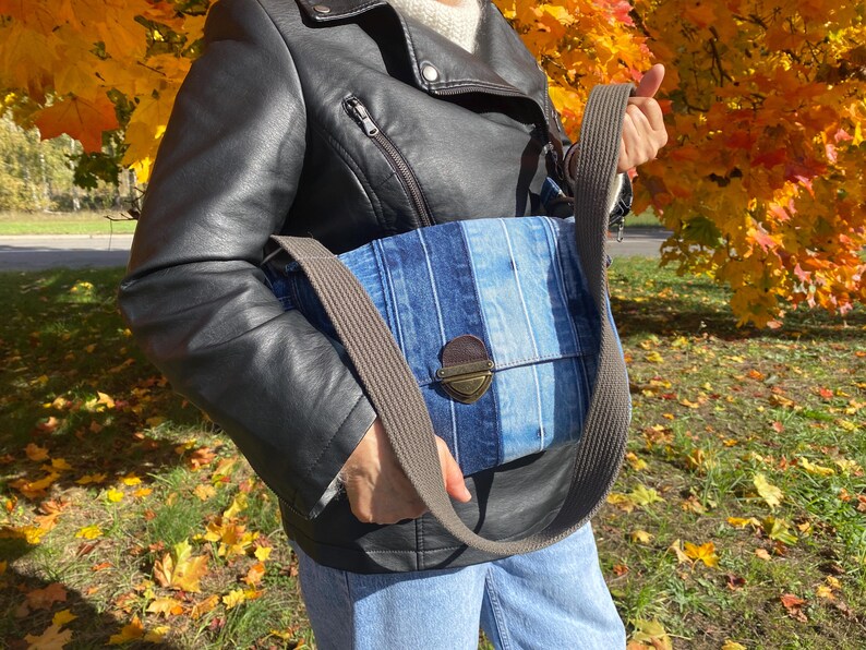 Upcycled denim messenger bag with striped design, adjustable strap, black nylon lining, and 2 interior pockets.
