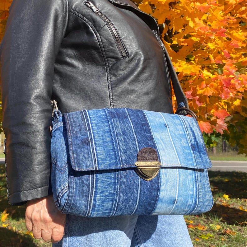 Upcycled denim messenger bag with striped design, adjustable strap, black nylon lining, and 2 interior pockets.
