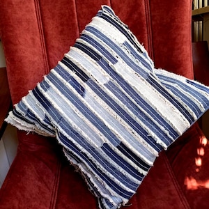 Può includere: Due cuscini quadrati con un design patchwork in tessuto denim blu, bianco e grigio. I cuscini hanno un bordo sfrangiato e sono appoggiati su una sedia di velluto rosso.