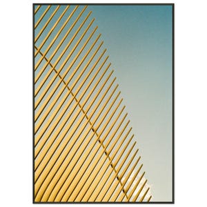 May include: Abstract art print featuring a geometric design of parallel yellow lines against a blue sky. The lines are arranged diagonally, creating a sense of depth and movement. The artwork is framed in a black border.