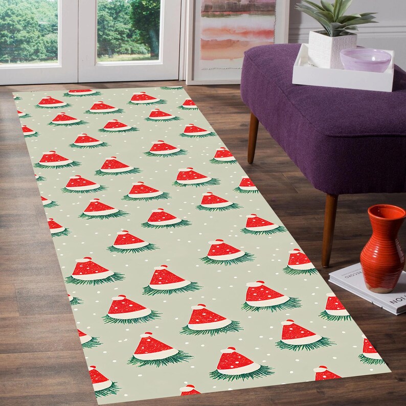 Op de afbeelding: Een rechthoekig vloerkleed met een herhalend patroon van rode kerstmutsen met witte randen en witte pompons, op een lichtgroene achtergrond met witte stippen. De hoeden zijn omgeven door groene dennennaalden.