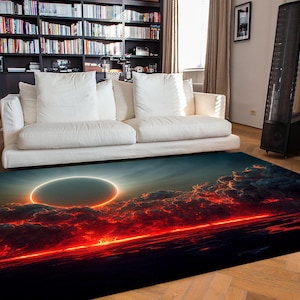 May include: A rectangular area rug featuring a vibrant celestial design. The rug showcases a fiery red and orange horizon with dark clouds and a bright, circular light source. The rug is placed in a living room setting with a white sofa and a bookshelf.