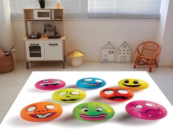Può includere: Una collezione di tappeti ovali colorati con facce di cartoni animati. Ogni tappeto presenta un'espressione diversa e colori vivaci, tra cui rosa, arancione, giallo, verde e blu. I tappeti sono disposti su una superficie bianca, creando un'atmosfera giocosa.