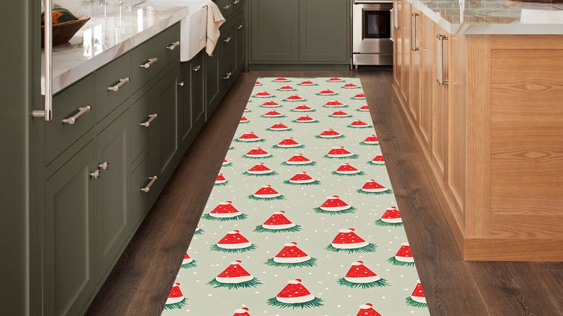 Op de afbeelding: Een rechthoekig loperkleed met een herhalend patroon van rode kerstmutsen op een lichtgroene achtergrond. De mutsen hebben witte randen en zijn omgeven door groene takjes en witte stippen. Het kleed ligt in een keuken.